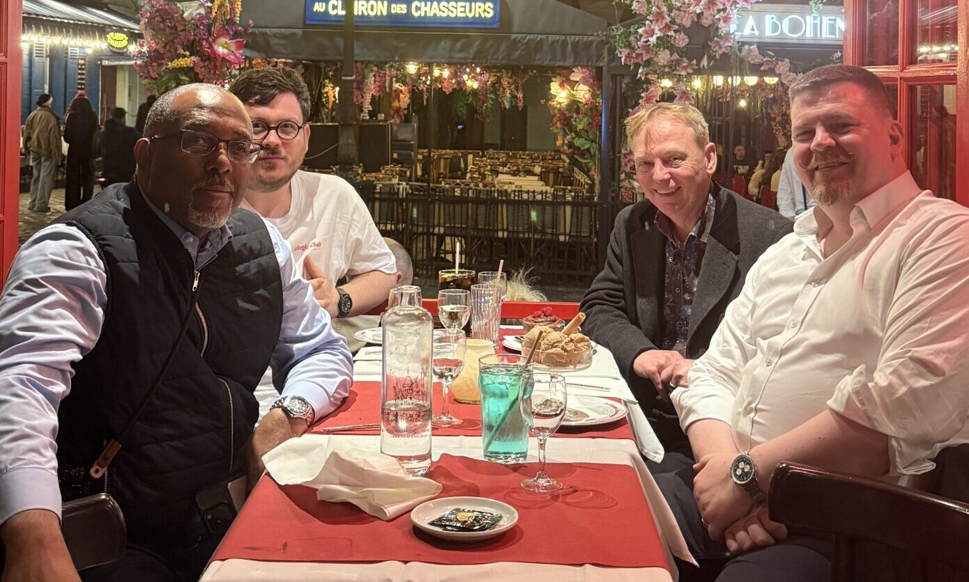 Corporate magician and host Liam Ball dining with performance experts Michael Vincent, Scott Penrose, and John Conway at a restaurant in Paris, France.