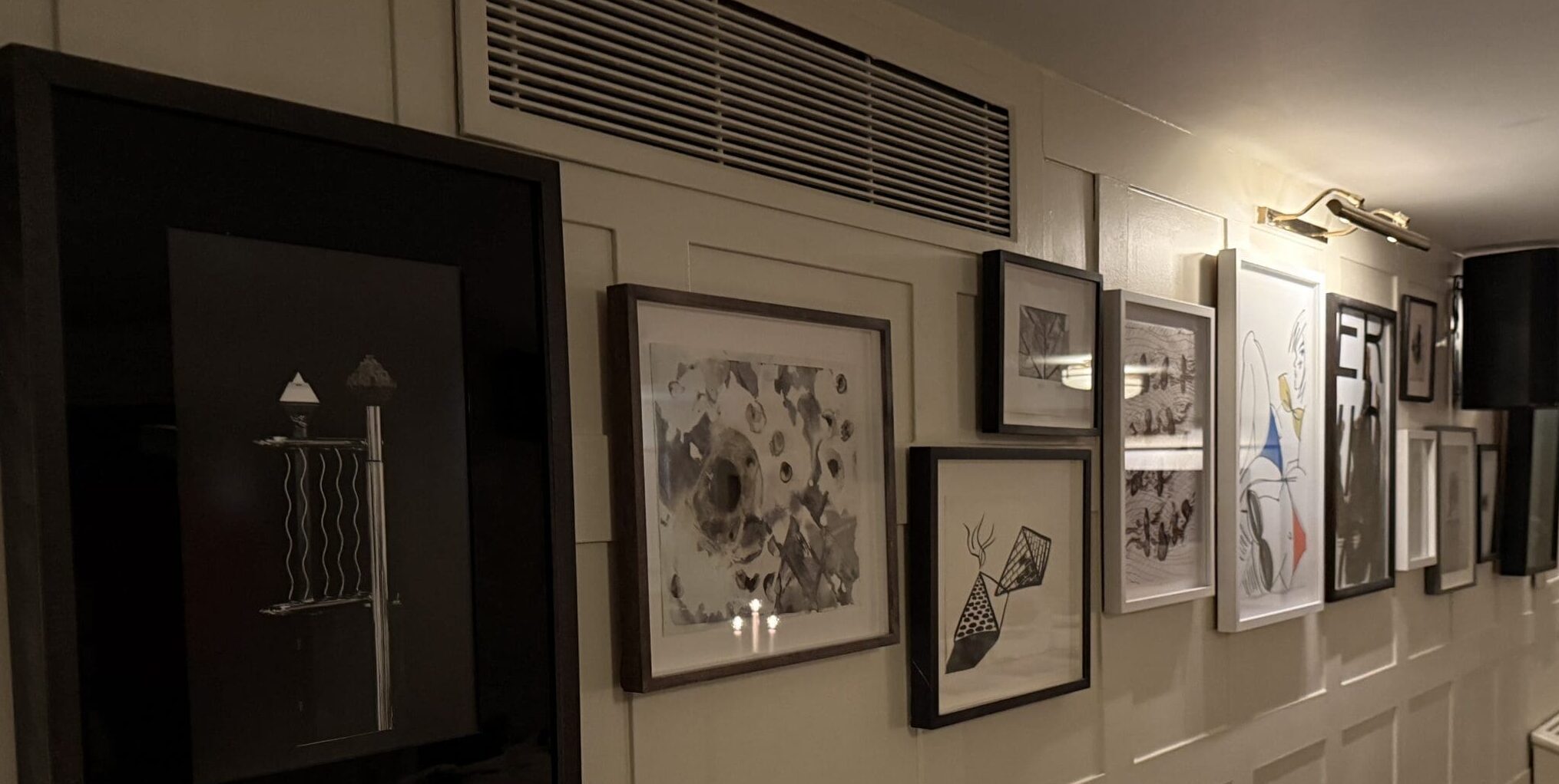 A gallery wall featuring framed monochrome modern artwork and wood-panelled walls inside High Road House, Chiswick.