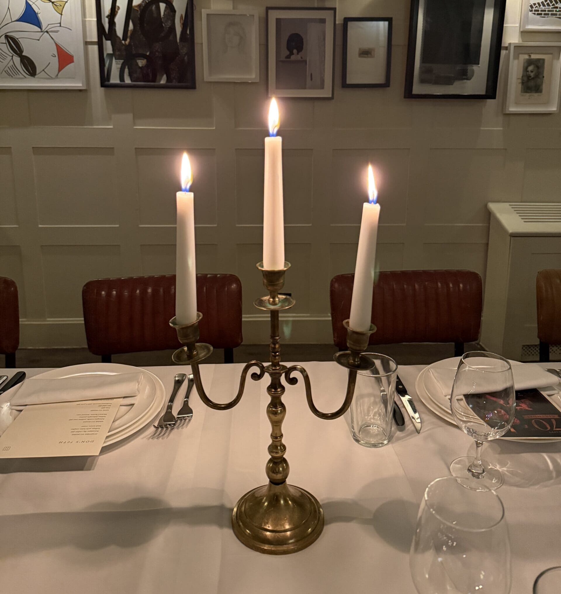 A Silver candelabra with three lit candles on a white tablecloth during a private party dinner at a Soho House club.